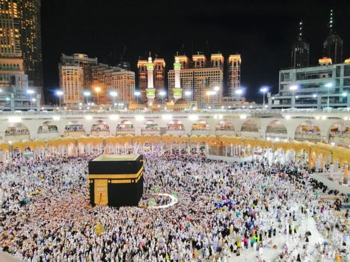 Aerial view of the Kaaba surrounded by pilgrims in Makkah at night, showcasing a religious gathering.